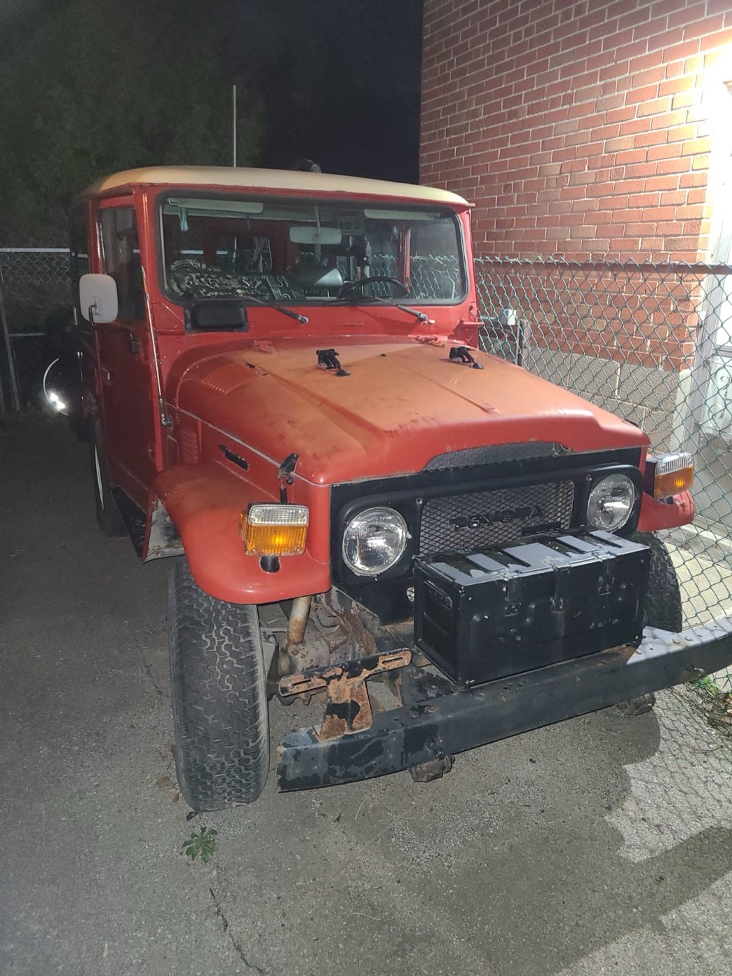 Orange BJ40 parked at night beside a brick wall