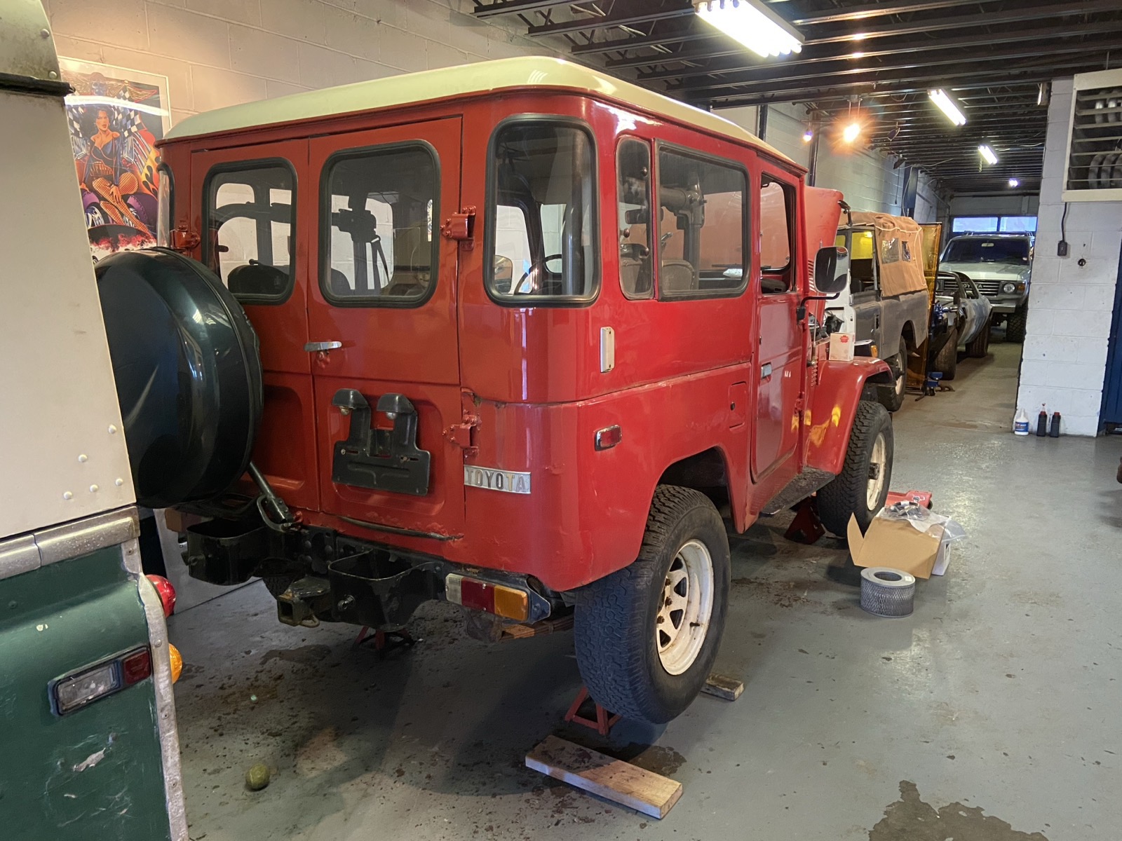 Red Toyota Land Cruiser BJ40 with spare tire on the rear door, in a workshop