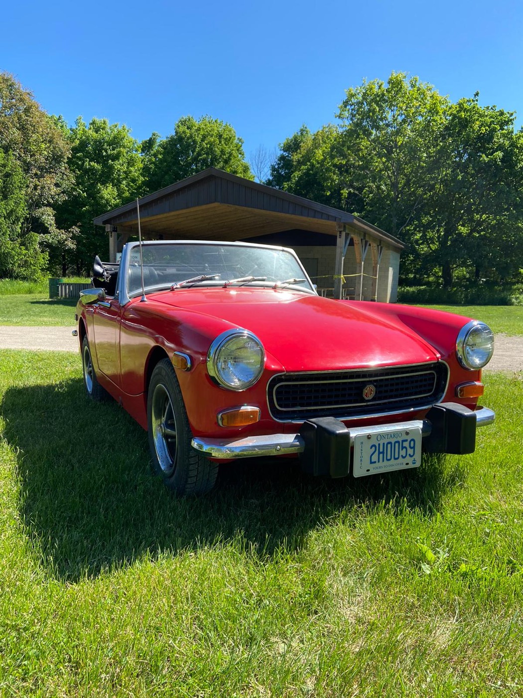 Red 1974 MG Midget on a lawn in front of a barn